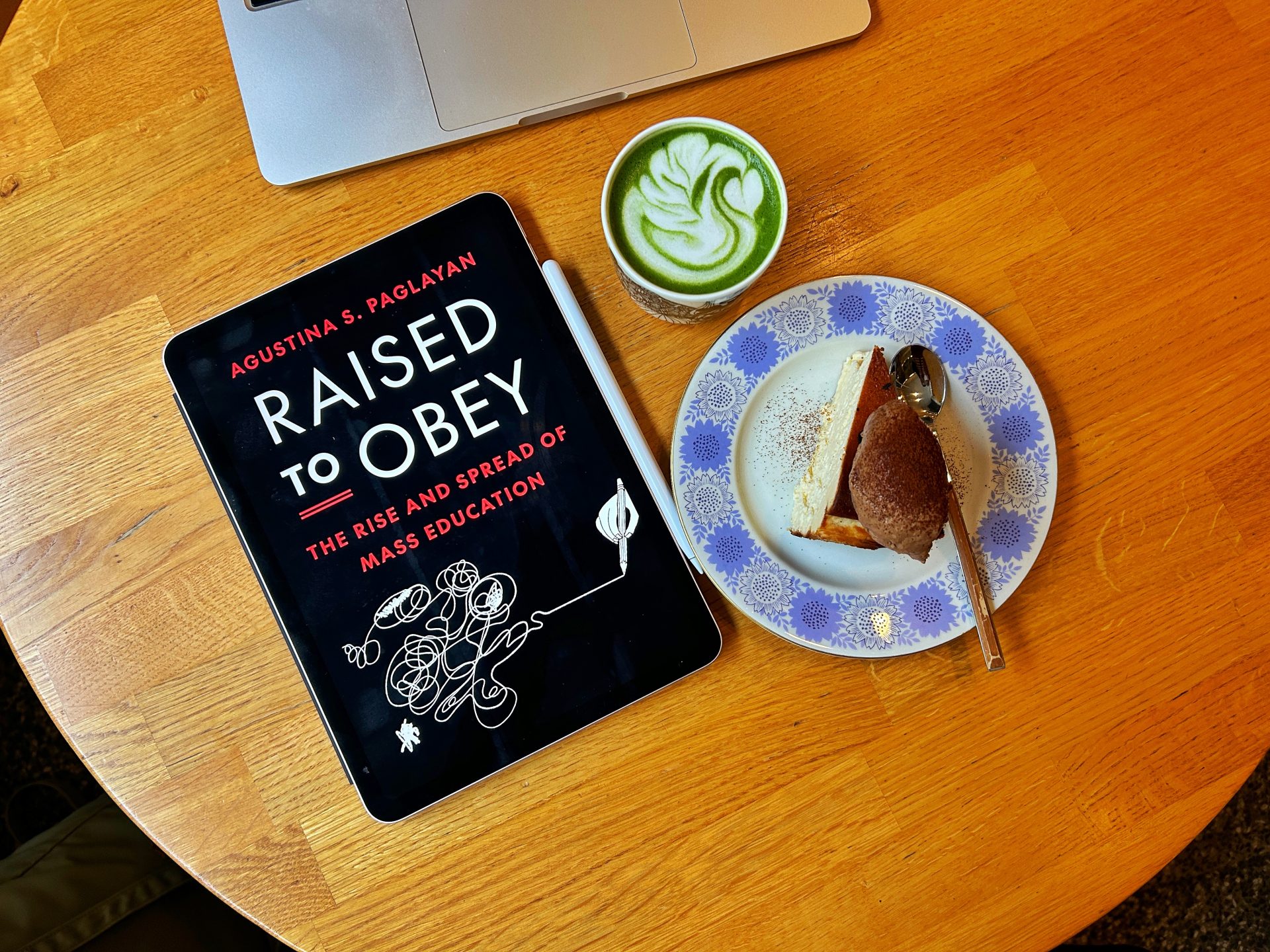 Raised to Obey ebook on a table with a cup of matcha and a slice of cake