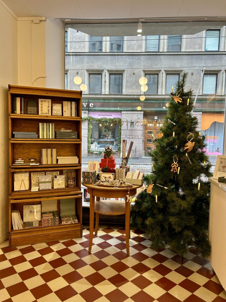 A shelf full on notebook, a table with some papers and stationary, and a christmas tree by the window