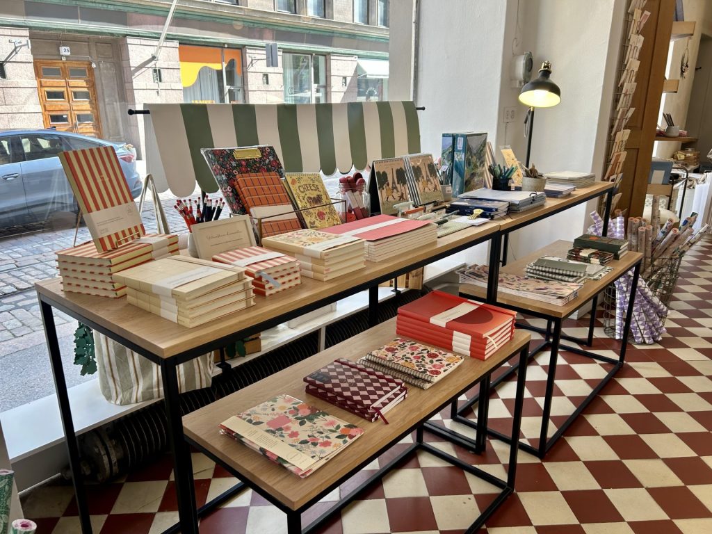 Table full of notebooks and some pens for journaling in a papershop with the background of street view outside the shop.