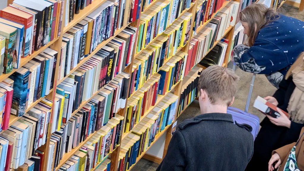 A man and a woman in front of a book shelves reading book covers.