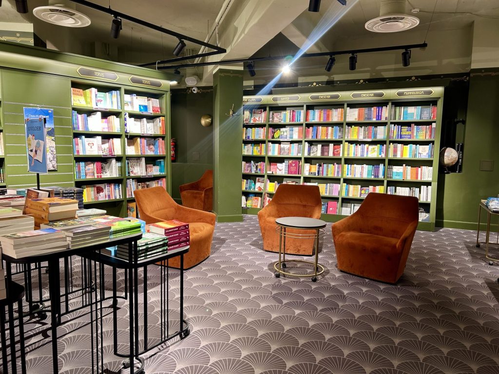 A corner in a bookstore consists of bookshelves, chairs, and some tables.
