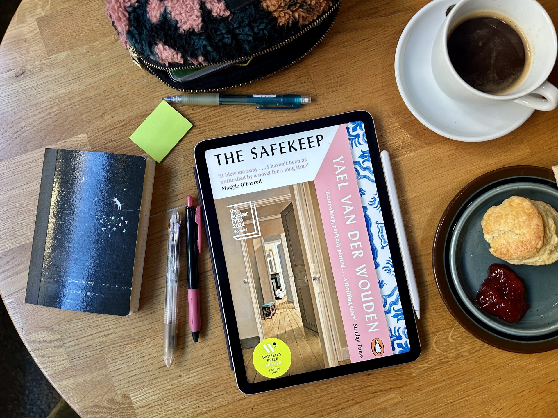 The Safekeep eBook on a wooden table surrounded by stationery and a notebook, with a cup of black coffee and a scone.