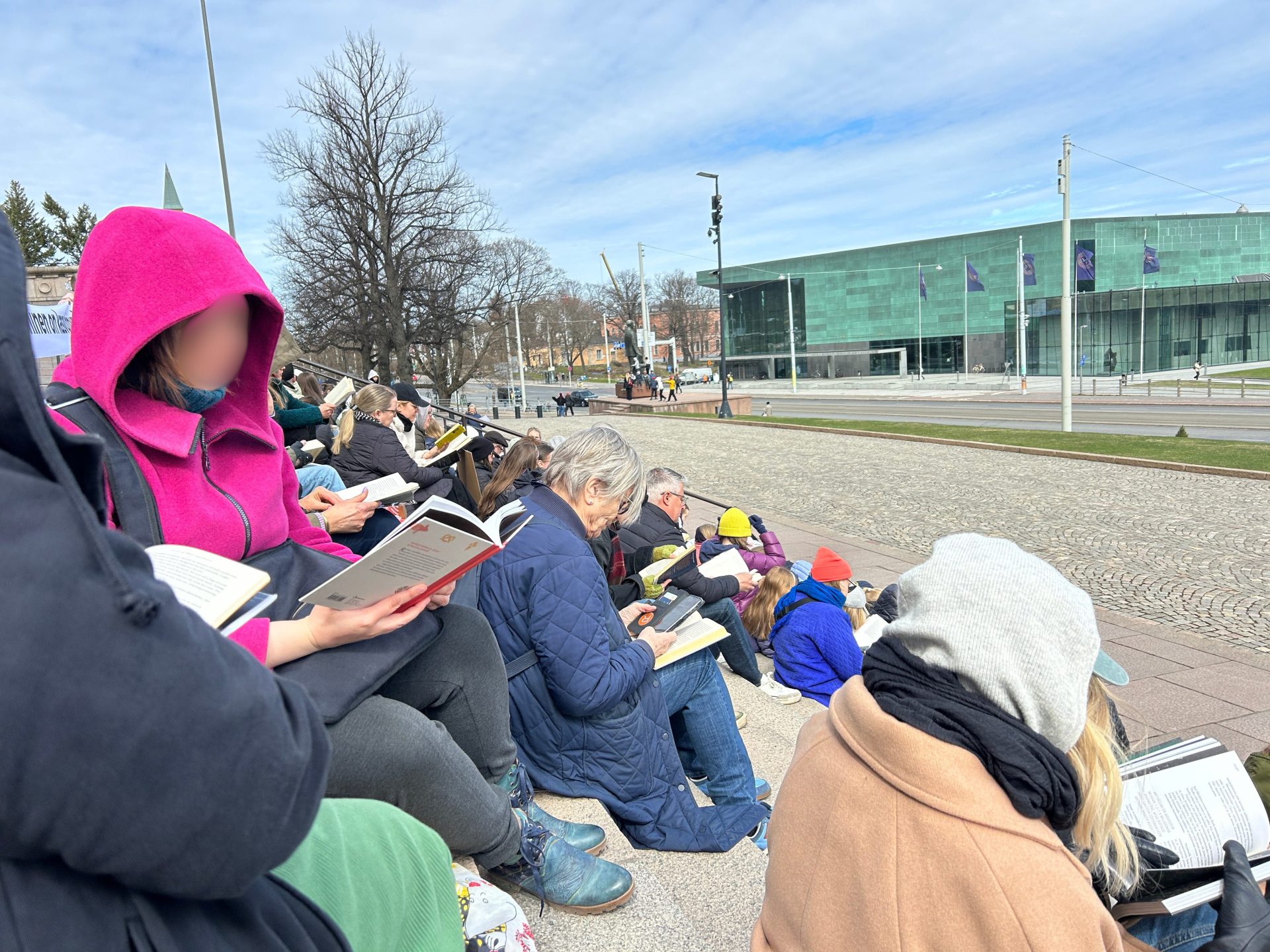 People of all ages sitting on outdoor stairs reading books together