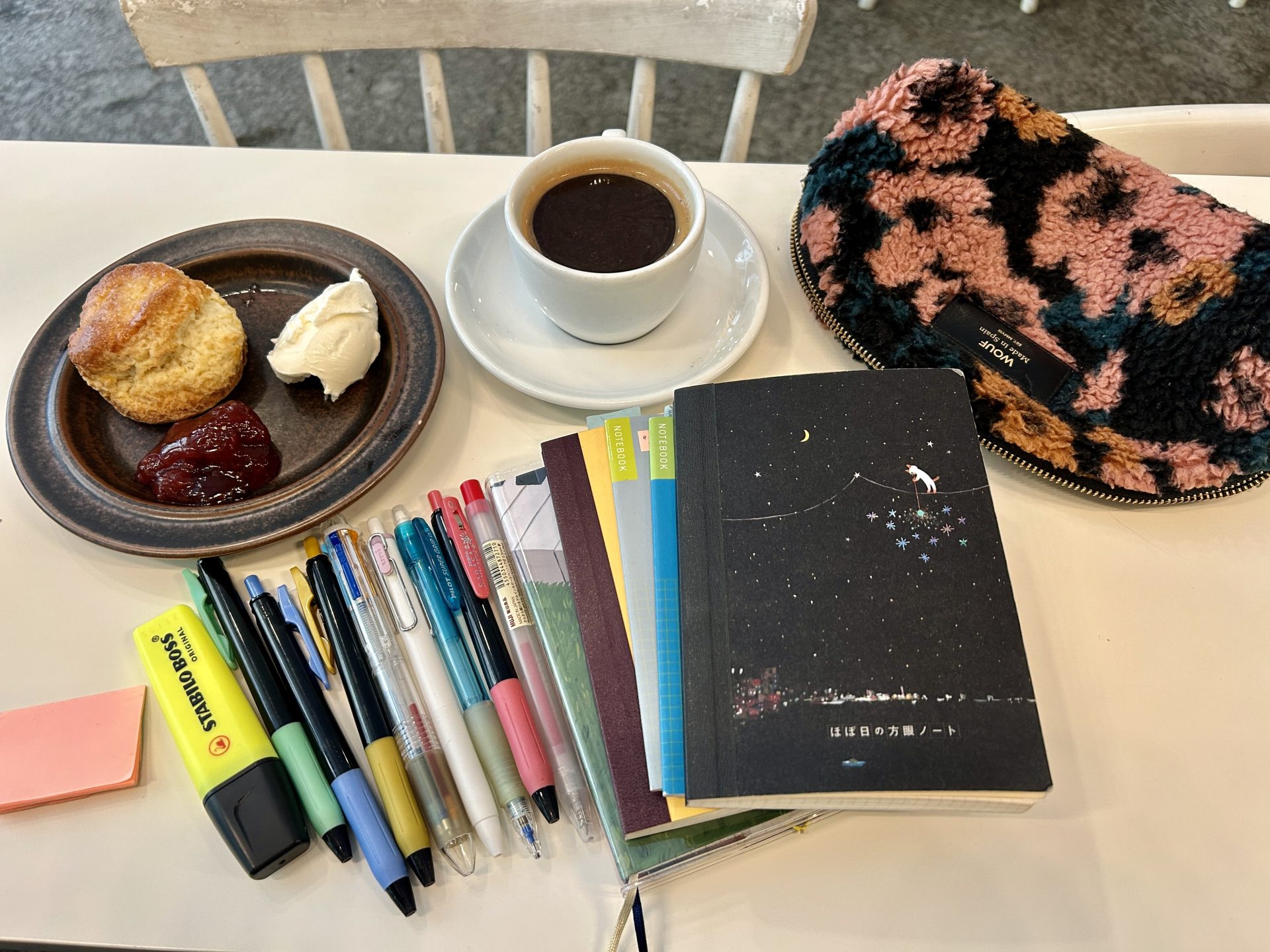 Stack of notebooks and lines of stationery with a cup of coffee and a scone on a white table