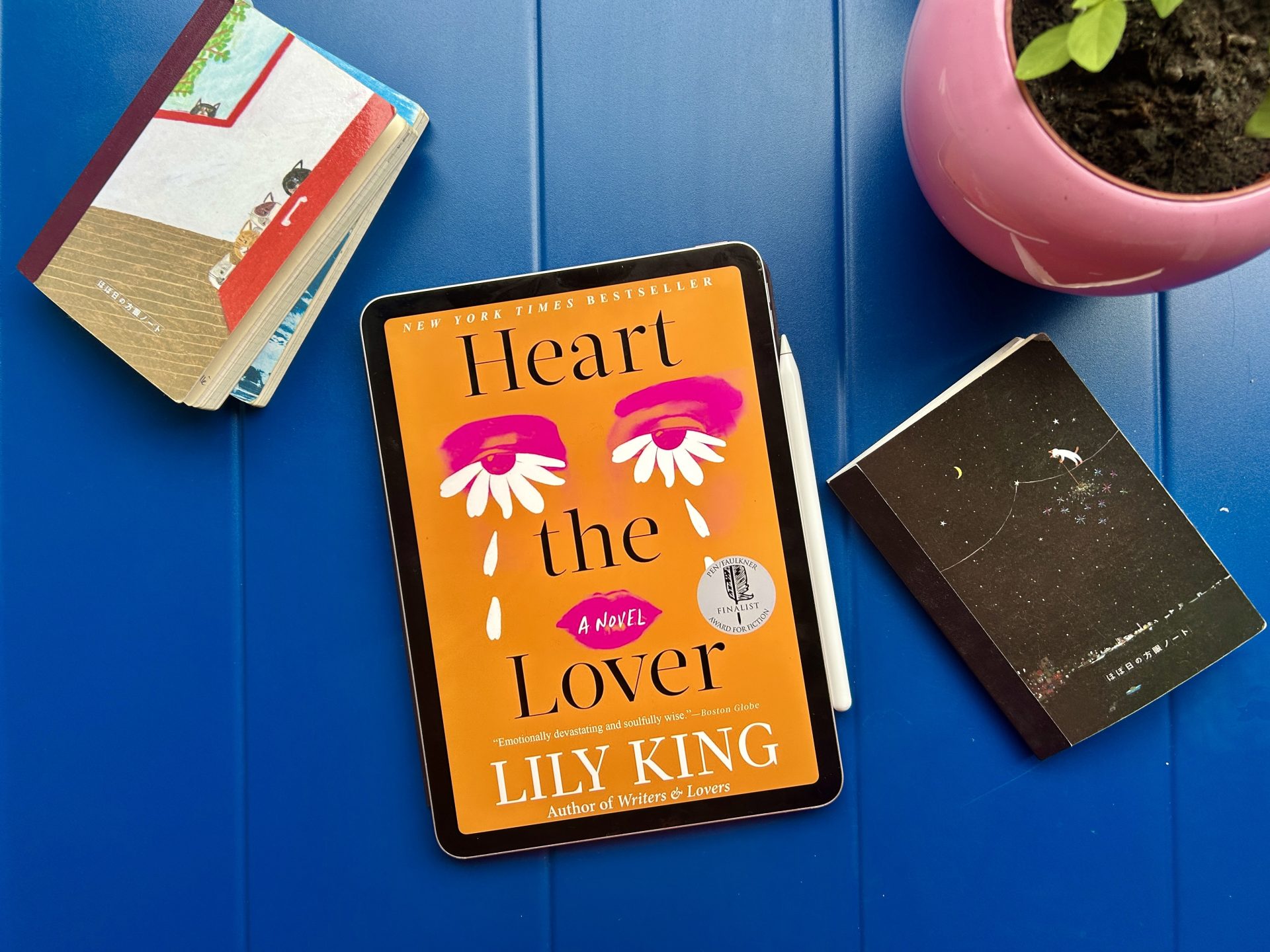 Heart the Lover eBook on a solid color table with some notebooks and a pot of plant