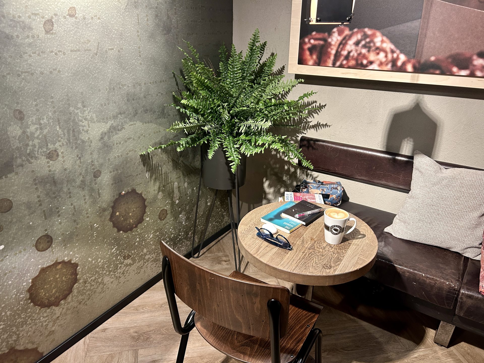 A chair, a plant, and a table full of books and a cup of coffee on the cafe corner
