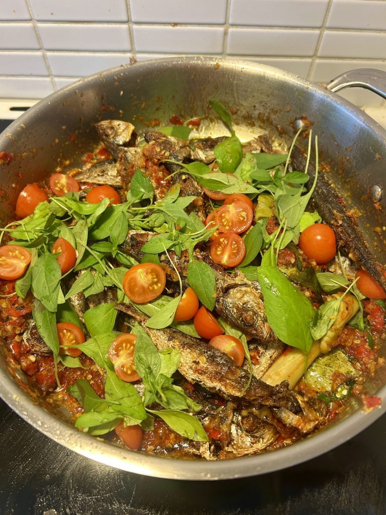 A pan of spicy fish with basil and tomatoes as topping